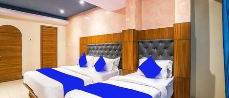 Habitación de hotel con dos camas, cada una con cabecero capitonado, ropa blanca y almohadas de color azul.