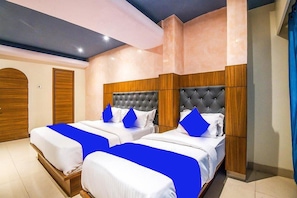 A hotel room with two beds, each with a tufted headboard, white bedding, and blue accent pillows. - Hotel Suites Inn (Mumbai)