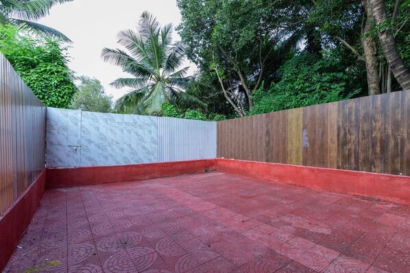 A courtyard with a red tiled floor, a white wall with a textured pattern, and a wooden wall with a reddish-brown finish.
