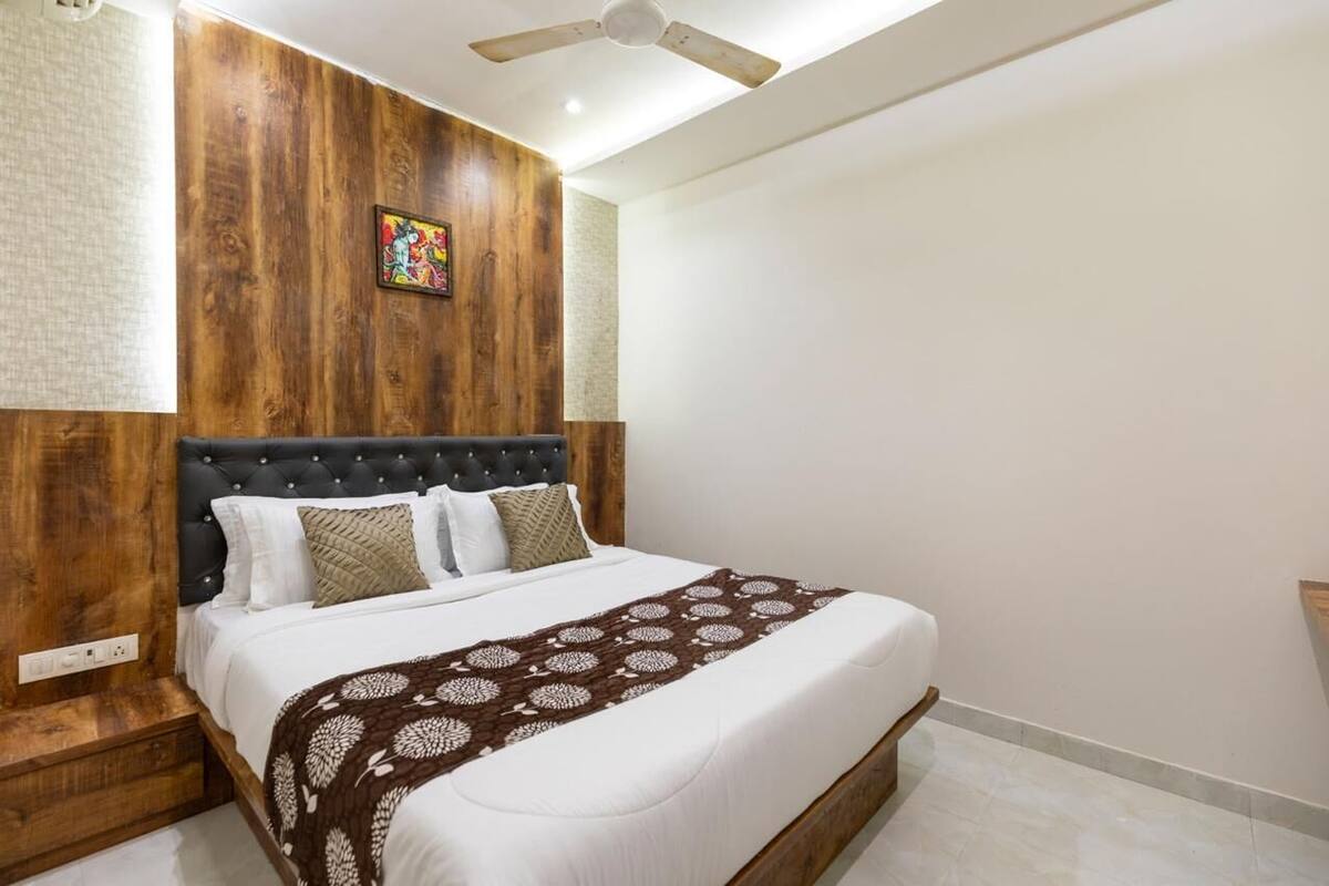 A bedroom with a wooden headboard, a bed with white bedding, a brown patterned throw, and a ceiling fan.