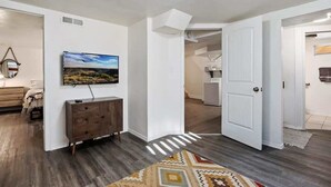 Een ruime woonkamer met een grote flatscreen televisie aan de muur, een houten kast en een kamerbreed tapijt.