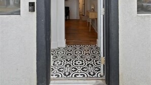 Ein moderner Eingangsbereich mit einer Tür in Schwarz, einer Fußmatte mit der Aufschrift „BE OUR GUEST“ und einem gemusterten Boden, der zum Innenbereich führt.