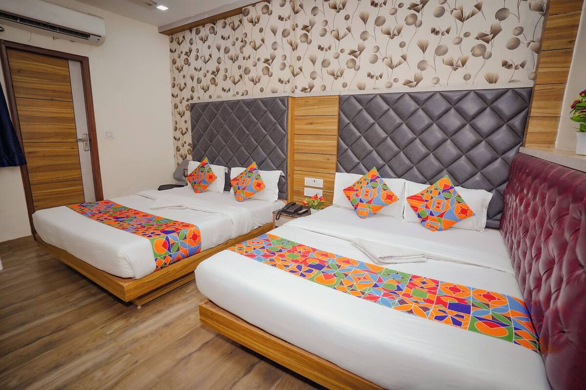 Ein Hotelzimmer mit zwei Betten, Holzboden, einem gemusterten Wandbild und einem roten, gepolsterten Kopfteil.