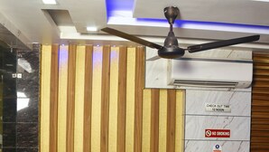 A reception area with a dark leather sofa, a ceiling fan, and a wall-mounted air conditioner. - Hotel Delhi Darshan -By RSL Hospitality (New Delhi)