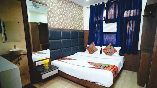 A hotel room with a bed, a bedside table, a mirror, a sink, and a window with curtains. - Hotel Delhi Darshan -By RSL Hospitality (New Delhi)