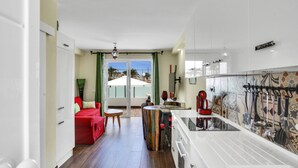 A modern kitchen with white cabinets, a dining area with a red sofa, and a view of the outdoors through a glass door. - CASA DEL SOL, Beautiful Terrace, Fast Wi-Fi, Pool (COSTA ADEJE)