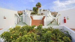 A modern hotel with a central staircase leading to upper floors, surrounded by lush greenery and white walls. - CASA DEL SOL, Beautiful Terrace, Fast Wi-Fi, Pool (COSTA ADEJE)
