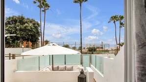 A balcony with a white umbrella, a cushioned seating area, and a view of palm trees and buildings. - CASA DEL SOL, Beautiful Terrace, Fast Wi-Fi, Pool (COSTA ADEJE)