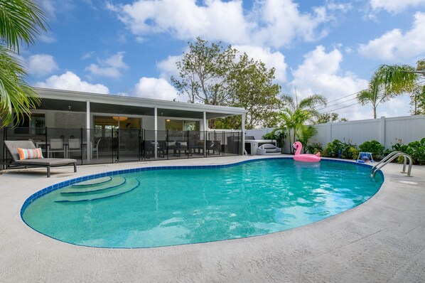 A swimming pool with a lounge area, a covered patio, and a view of the sky.