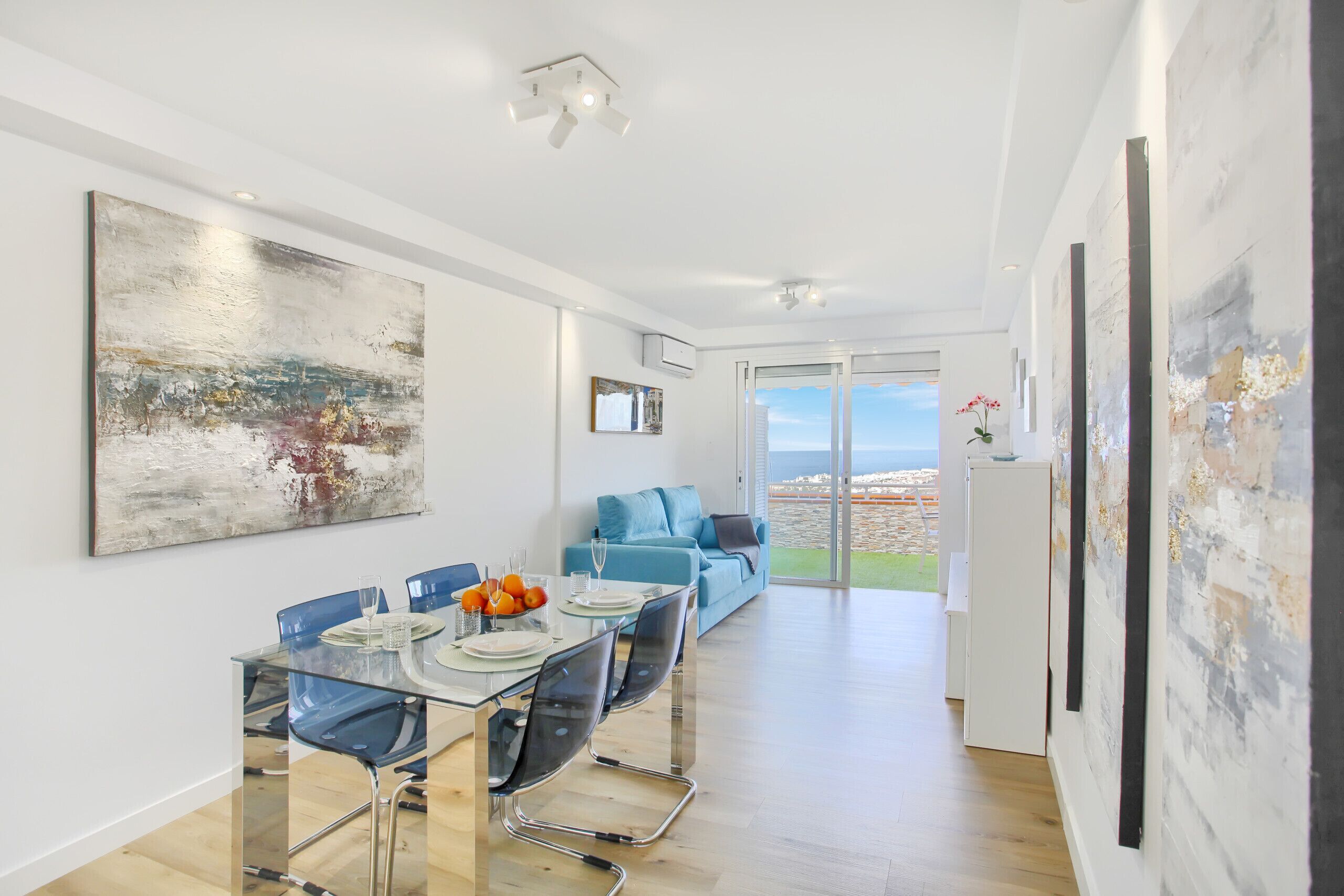 A modern dining area with a glass table, blue chairs, and a view of the outdoors.