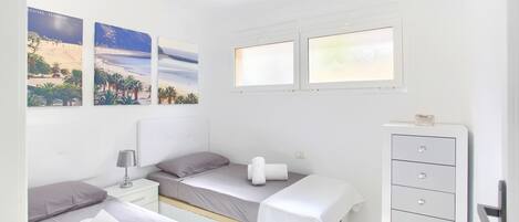 Une chambre avec deux lits simples, une table de chevet avec une lampe, une commode et trois tableaux encadrés accrochés au mur.