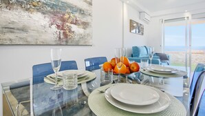 A dining area with a glass table set for four, a bowl of oranges, and a large abstract painting on the wall. - The Penthouse, Fabulous Sunset, Heated Pool, Fiber (Costa Adeje)