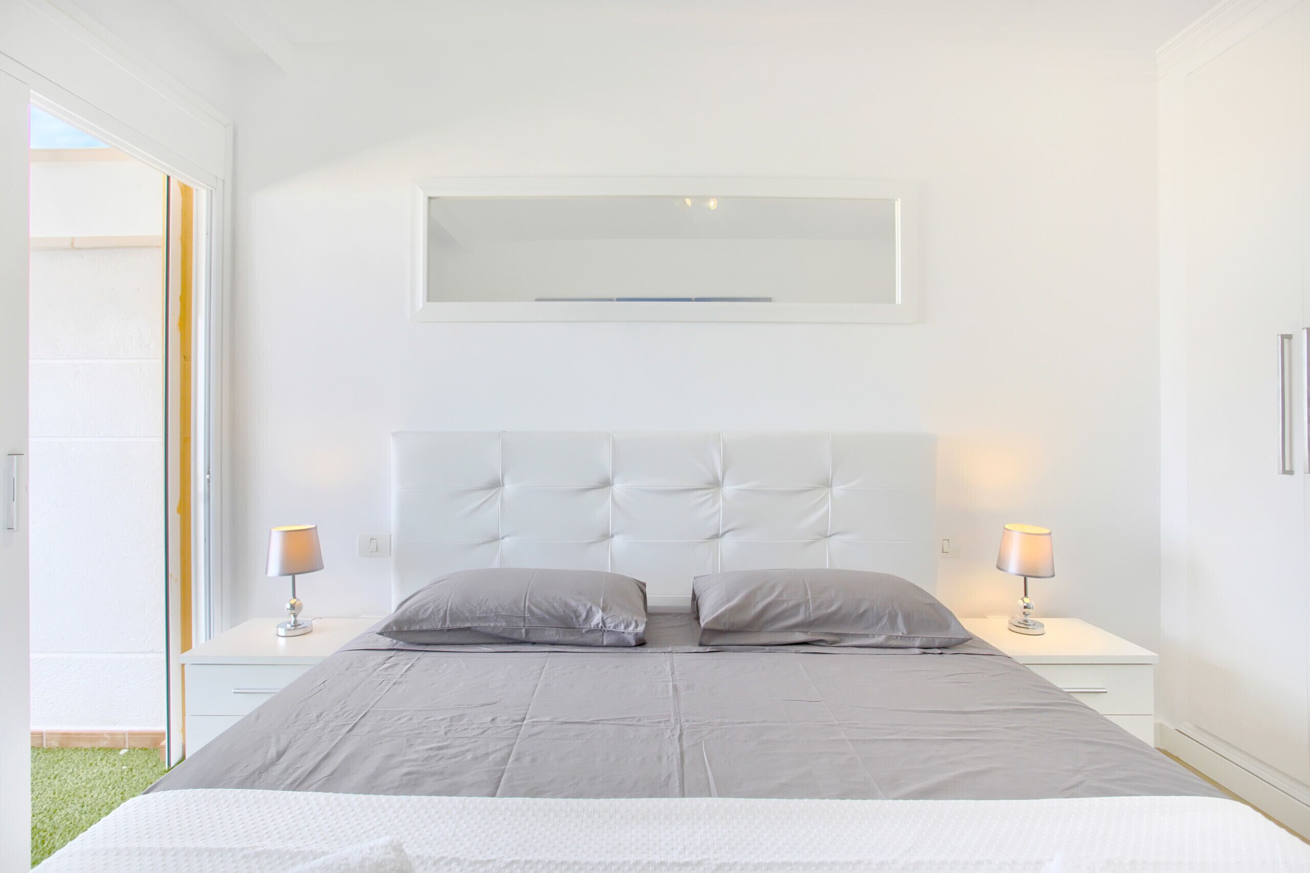 Ein modernes Schlafzimmer mit einem großen Bett, zwei Nachttischen und einem Fenster mit Blick ins Freie.