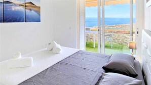 A hotel room with a bed, a towel, a lamp, and a view of the sea and cityscape. - The Penthouse, Fabulous Sunset, Heated Pool, Fiber (Costa Adeje)