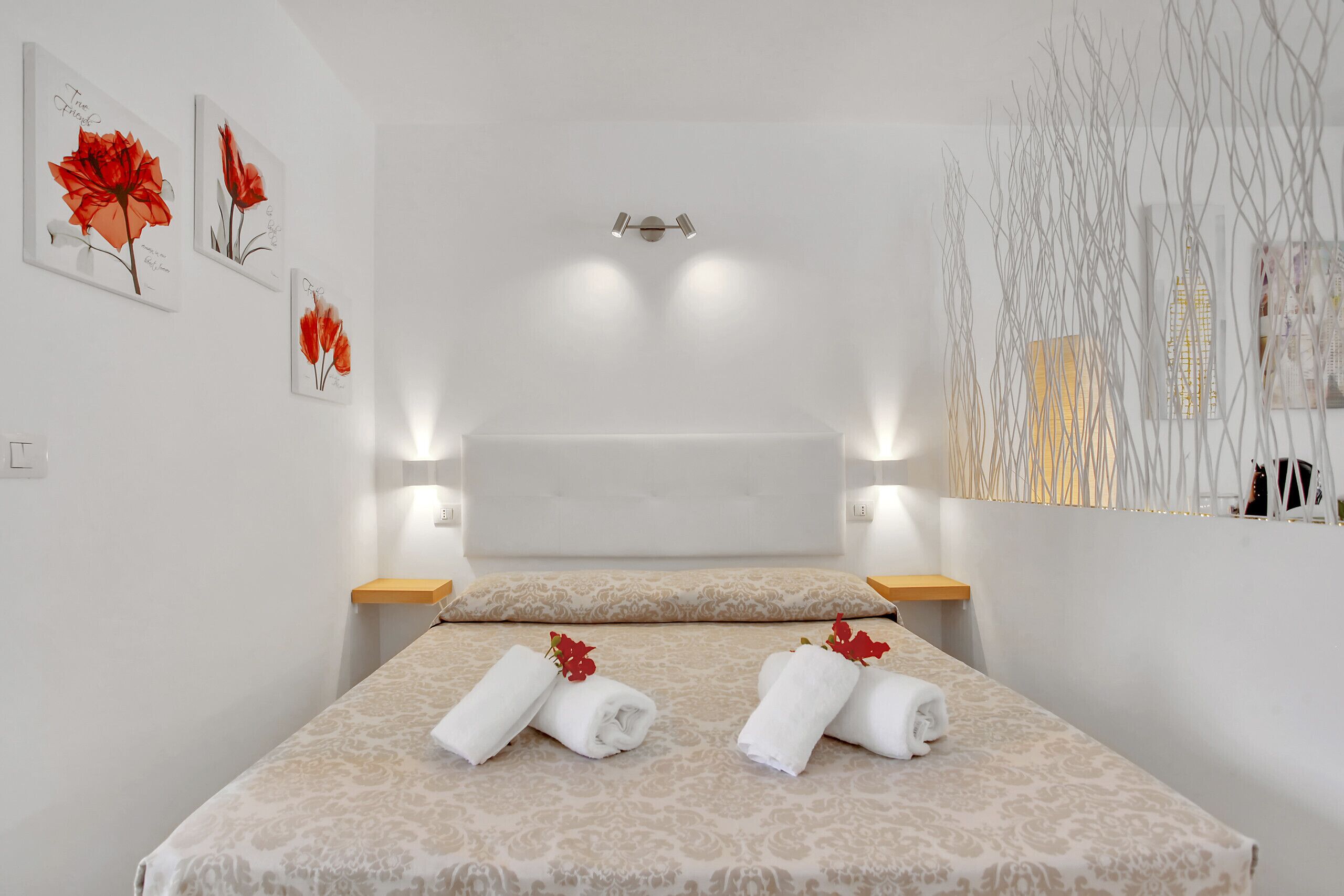 Habitació d'hotel amb un llit, dues làmpades de paret, un mirall i obra d'art.