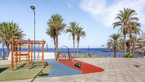 A playground with a slide and climbing structures, palm trees, and a view of the sea. - Ocean Touch Studio, Pool, Wi-Fi, Near the Beach (Playa de Las Americas)