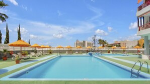 A swimming pool with lounge chairs and umbrellas, surrounded by a white fence and palm trees. - Ocean Touch Studio, Pool, Wi-Fi, Near the Beach (Playa de Las Americas)