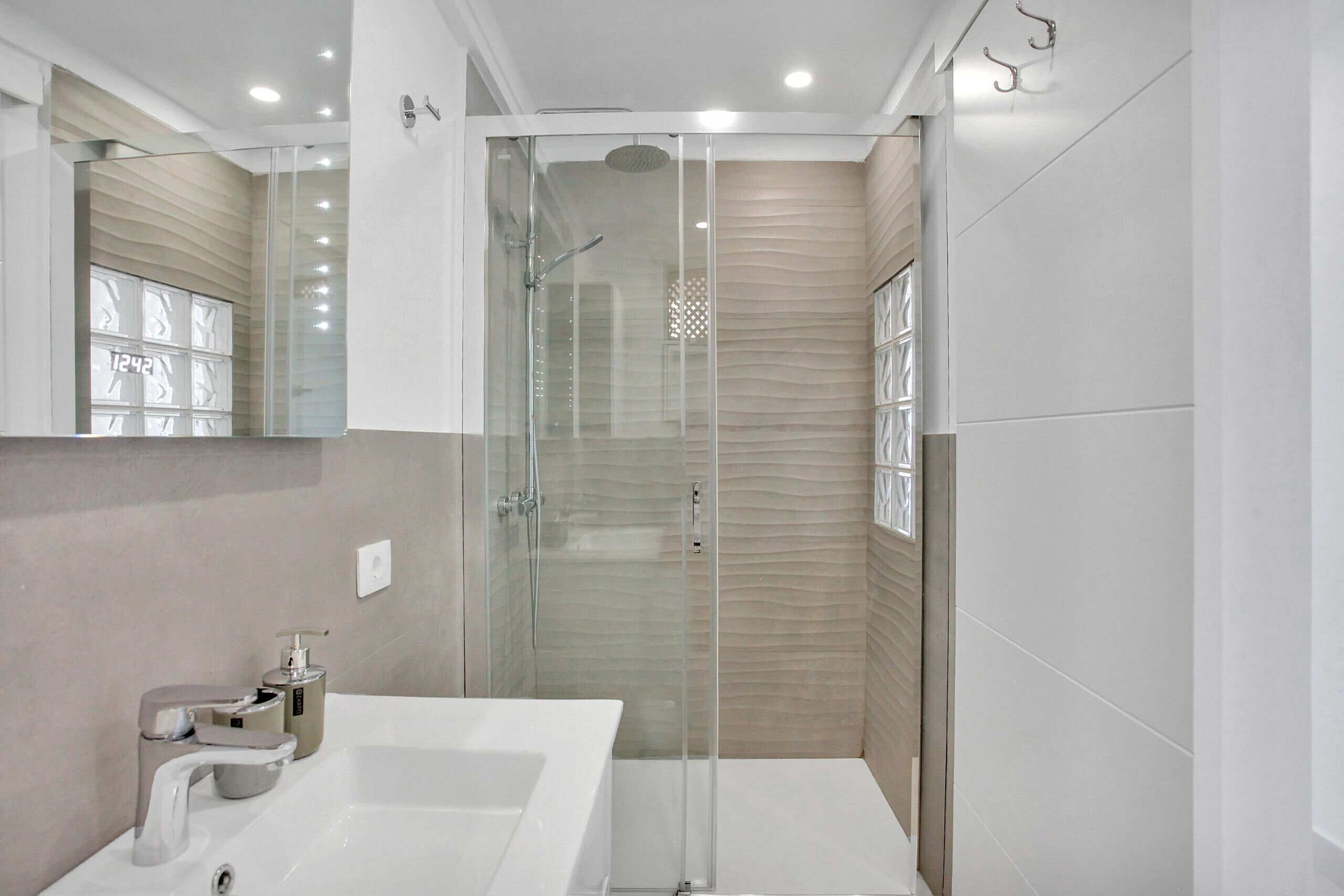 A modern bathroom with a glass-enclosed shower, a white sink, and a mirror above it.