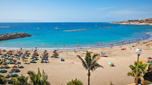 A beach with umbrellas, people, and a clear blue sky.