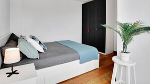 A bedroom with a bed, bedside table, lamp, and a potted plant.