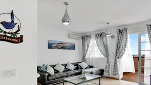 Un salon moderne avec un canapé, une table basse et un tableau représentant une ville côtière.