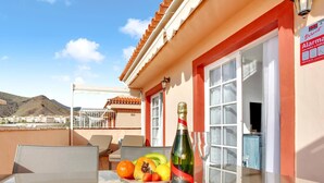 Un balcon avec une table dressée pour un repas, une bouteille de champagne et une vue sur les environs.