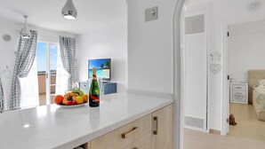 Une cuisine moderne avec un plan de travail blanc, une bouteille de champagne et un panier de fruits.