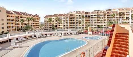 A resort with a large swimming pool, multiple balconies, and a clear sky.