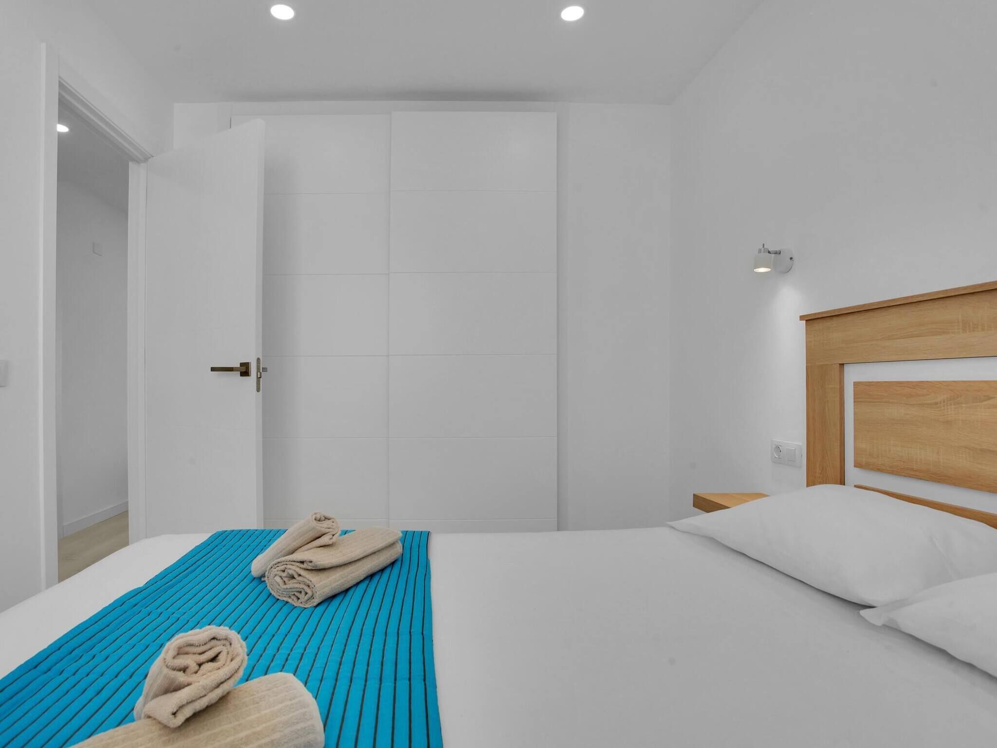 Una habitación de hotel moderna con una cama grande, un cabecero de madera y una decoración clara en tonos blancos.