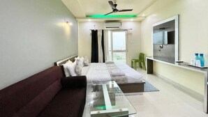 A modern bedroom with a glass coffee table, a bed with white linens, a ceiling fan, and a TV on the wall. - Hotel Trends - near Sea Beach & Temple (Puri)