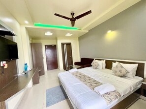 A hotel room with a bed, bedside table, TV, ceiling fan, and a bathroom door.