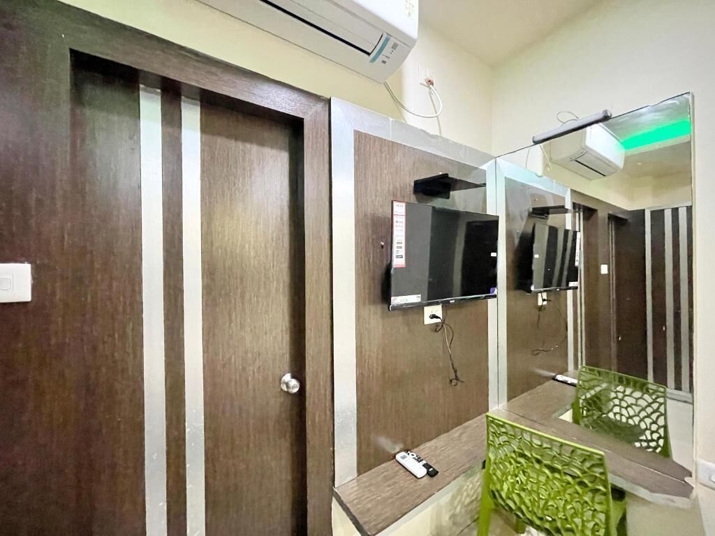A hotel room with a wooden door, a mounted TV, and a mirror reflecting the room.