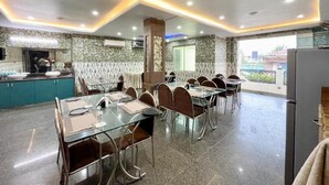 A dining area with glass tables and chairs, a kitchen in the background, and a view of the outside. - Hotel Trends - near Sea Beach & Temple (Puri)