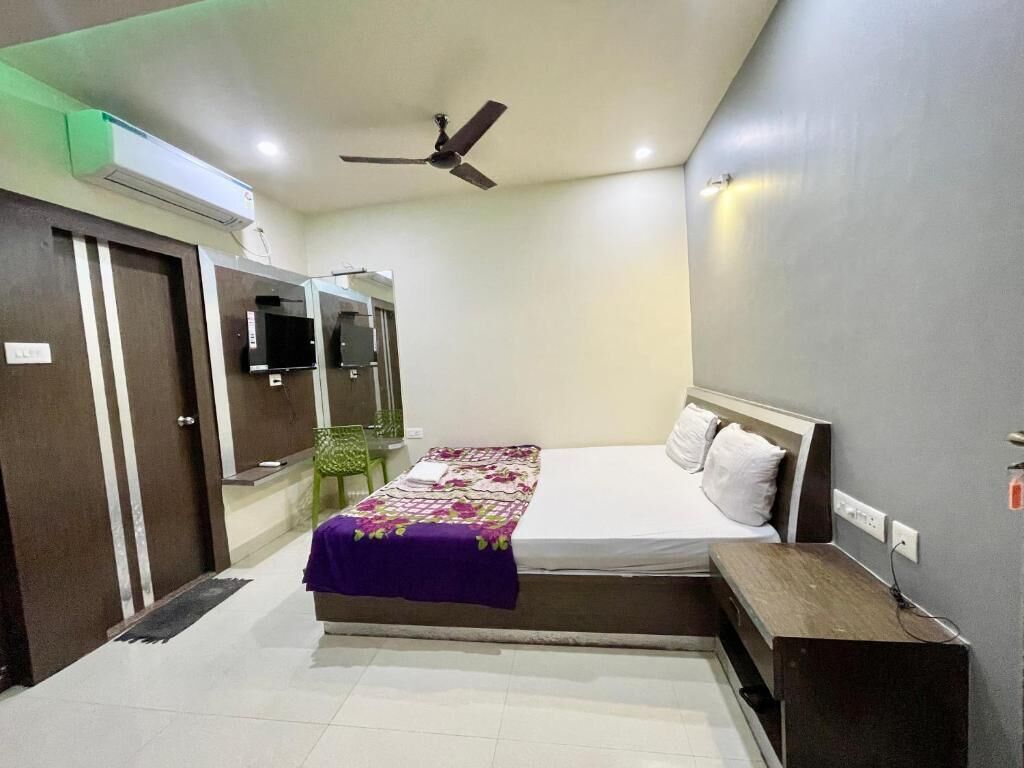 Una camera da letto con un letto, una ventola a soffitto, un televisore e una poltrona verde.