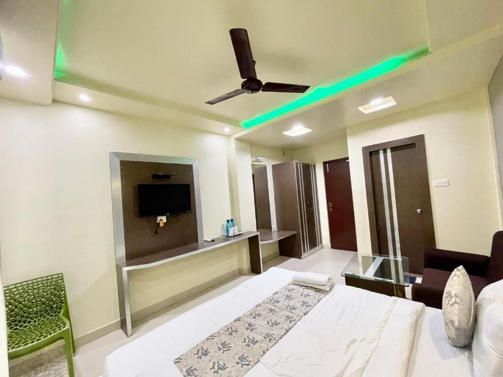 A hotel room with a bed, a TV mounted on the wall, a ceiling fan, and a desk with a chair.