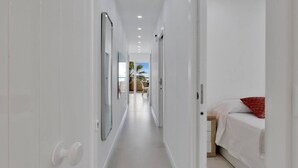 A narrow hallway with white walls and a tiled floor, leading to a bedroom with a bed and a red pillow. - Casa Marinita, Penthouse By The Sea (Arona)