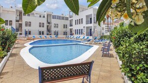 A swimming pool area with lounge chairs and a bench, surrounded by greenery and white buildings. - Ferdy's Home, Pool, Wi Fi, Downtown Los Cristianos (Los Cristianos)