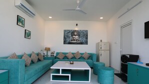 A modern living room with a teal sofa, a white coffee table, and a ceiling fan. - Banipark Service Apartment (Jaipur)