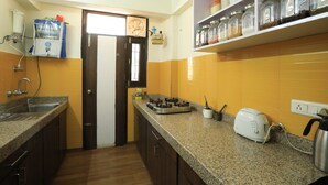A kitchen with granite countertops, a gas stove, a toaster, and a coffee maker. There are jars on a shelf above the counter. - Banipark Service Apartment (Jaipur)