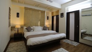 A bedroom with a bed, bedside lamps, a ceiling fan, and a large mirror. - Banipark Service Apartment (Jaipur)