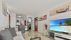 Sala de estar com televisão de tela plana, sofá, área de jantar e cozinha ao fundo.