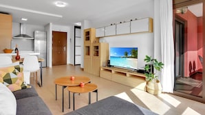 Un soggiorno moderno con TV a schermo piatto, divano, zona pranzo con tavolo e sedie e cucina completa di frigorifero e fornelli.