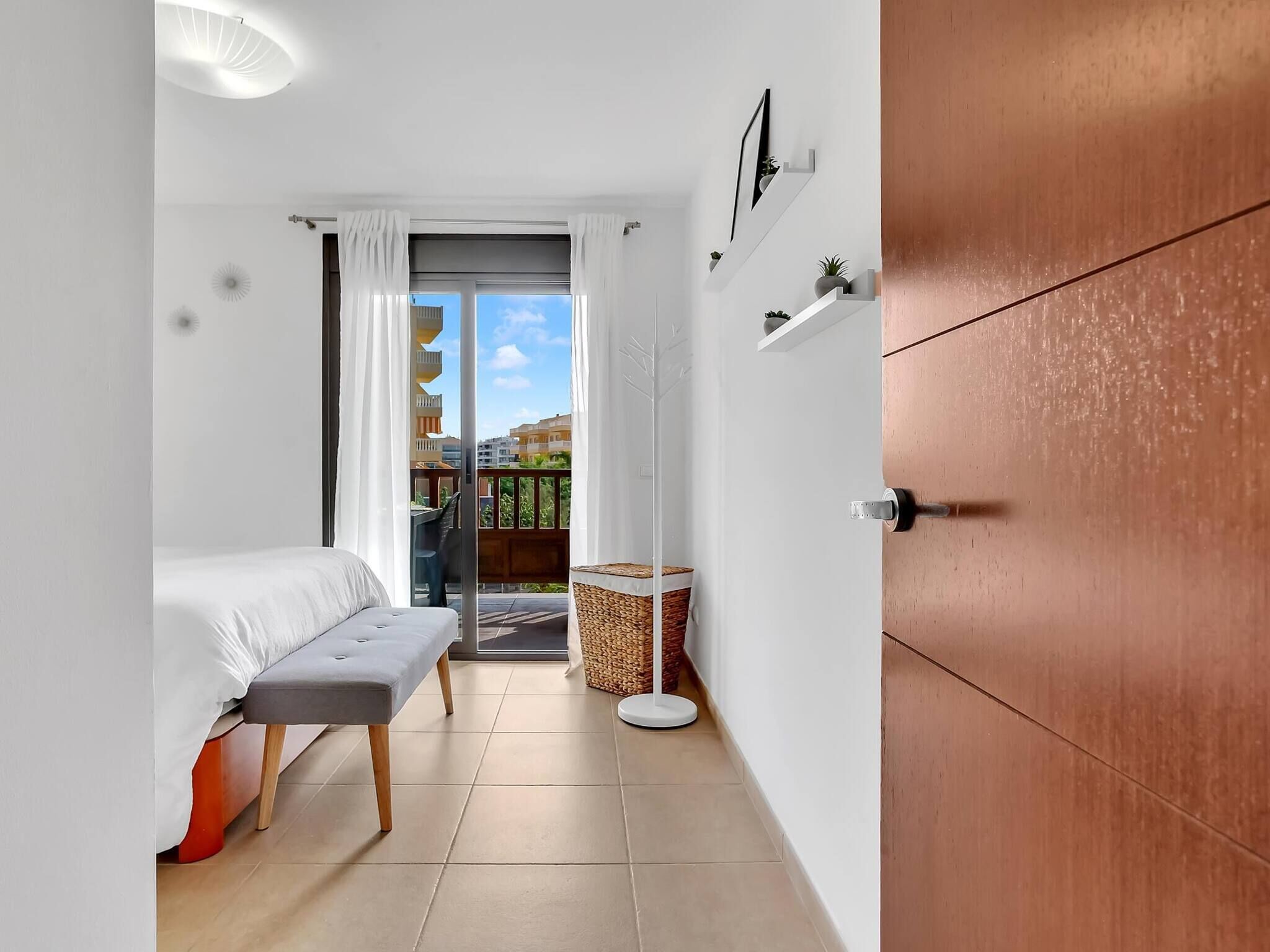 Un dormitorio moderno con cama, banco y vista al balcón.