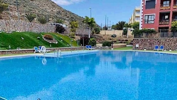 Una piscina con acqua azzurra, circondata da un muro in pietra e un edificio con balconi.