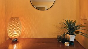 Een houten tafel met een structuurwand, een ronde spiegel, een lamp met een patroon en een potplant.