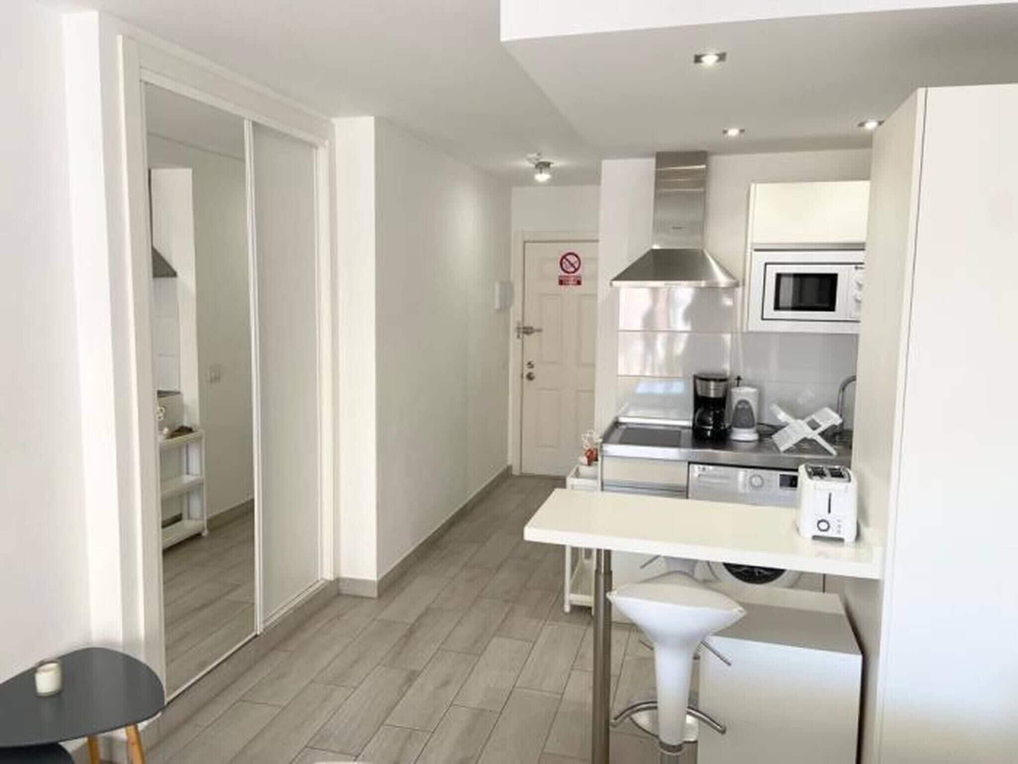 A modern kitchen with a microwave, coffee maker, and a small dining area with a white table and bar stool.