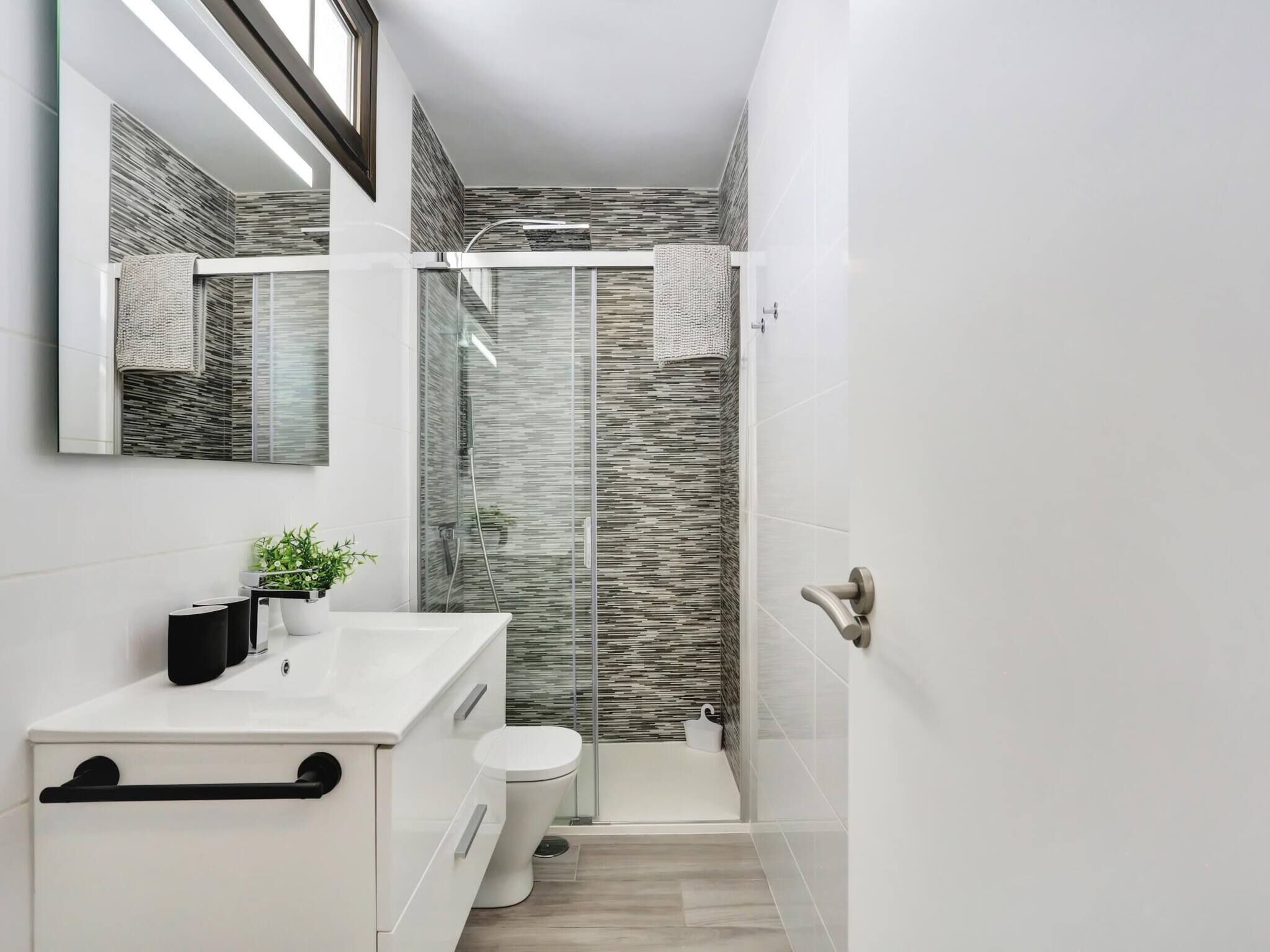 A modern bathroom with a glass shower enclosure, a white sink, and a toilet.