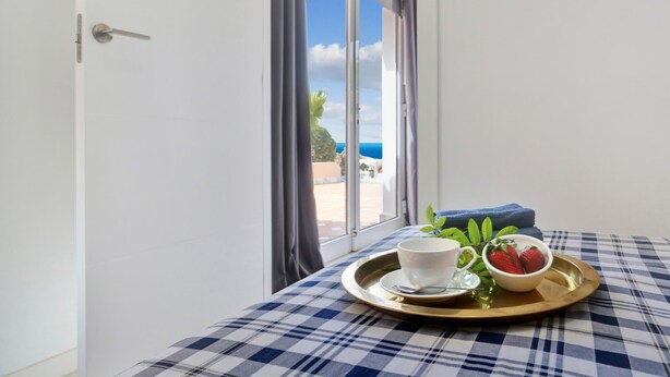 A room with a checkered tablecloth, a tray with a cup, a bowl of strawberries, and a view of the sea through a window. - The Stone Apartment, Los Gigantes, Heated Pool (Acantilados de Los Gigantes)