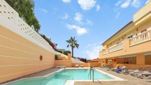 A swimming pool with lounge chairs and a lifebuoy on the wall. - The Stone Apartment, Los Gigantes, Heated Pool (Acantilados de Los Gigantes)