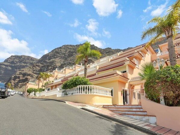 A coastal street with a row of buildings, a clear sky, and mountains in the background.